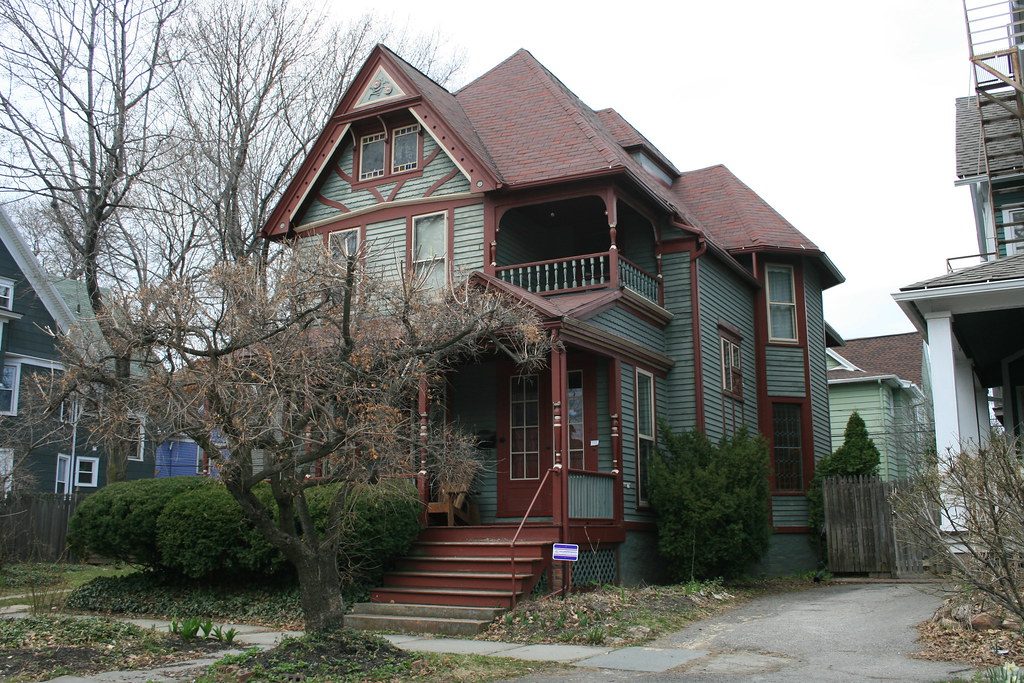 Victorian house with a red roof and a front porch on a residential street