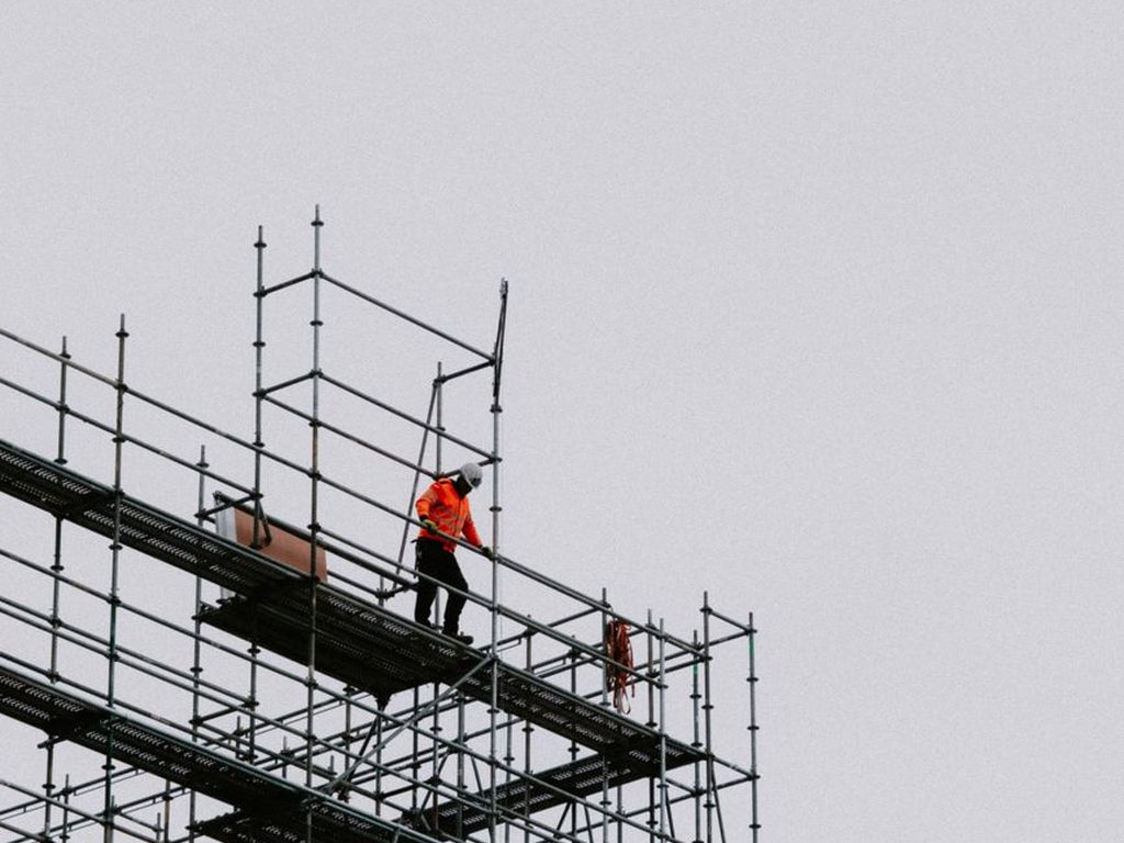 Worker on scaffolding high above the ground against a gray sky